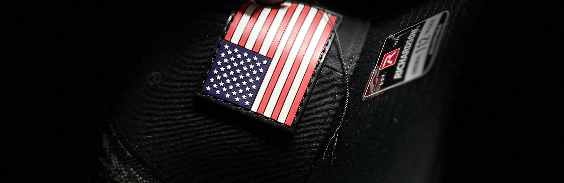 Black cap with American flag patch and text 'Machine Stitched & Glued' on a dark background